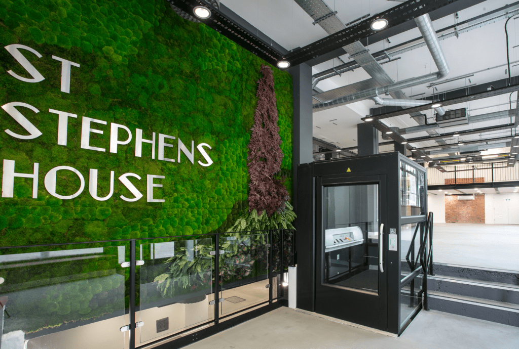 Office entrance with live moss wall and signage. There is a lift and a set of stairs.