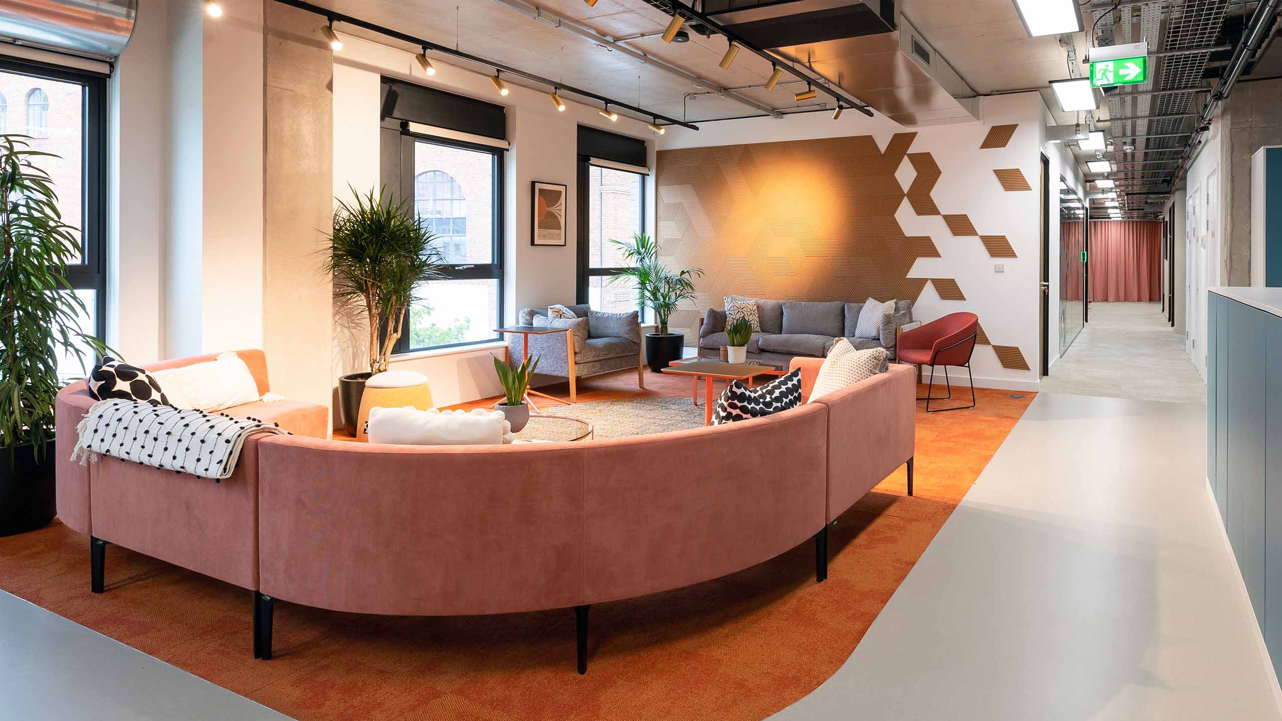 An office breakout space with large curved pink sofa and gold wall decal