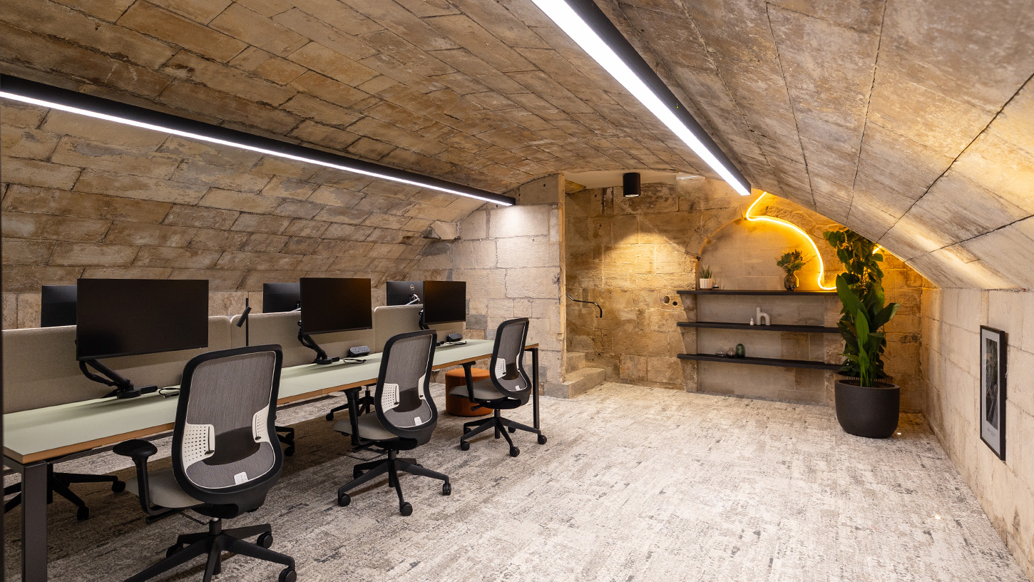 Office basement area with curved exposed brick ceiling, desks and neon wall light