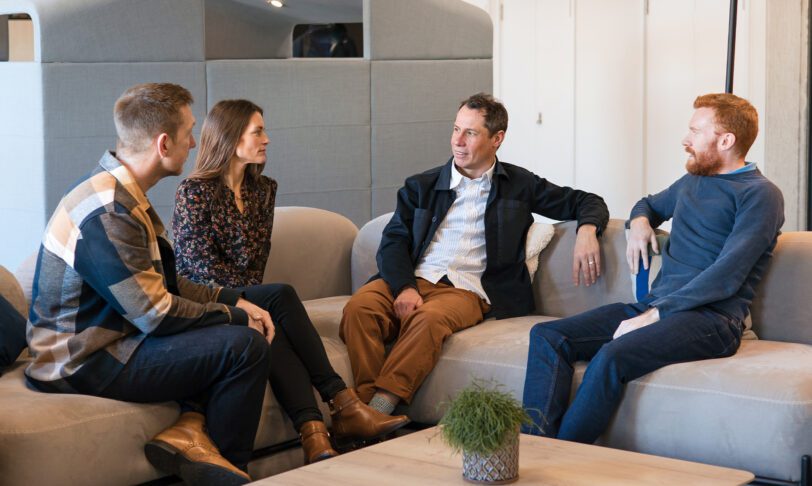 3 men and 1 women sitting on a sofa in a communal area of an office