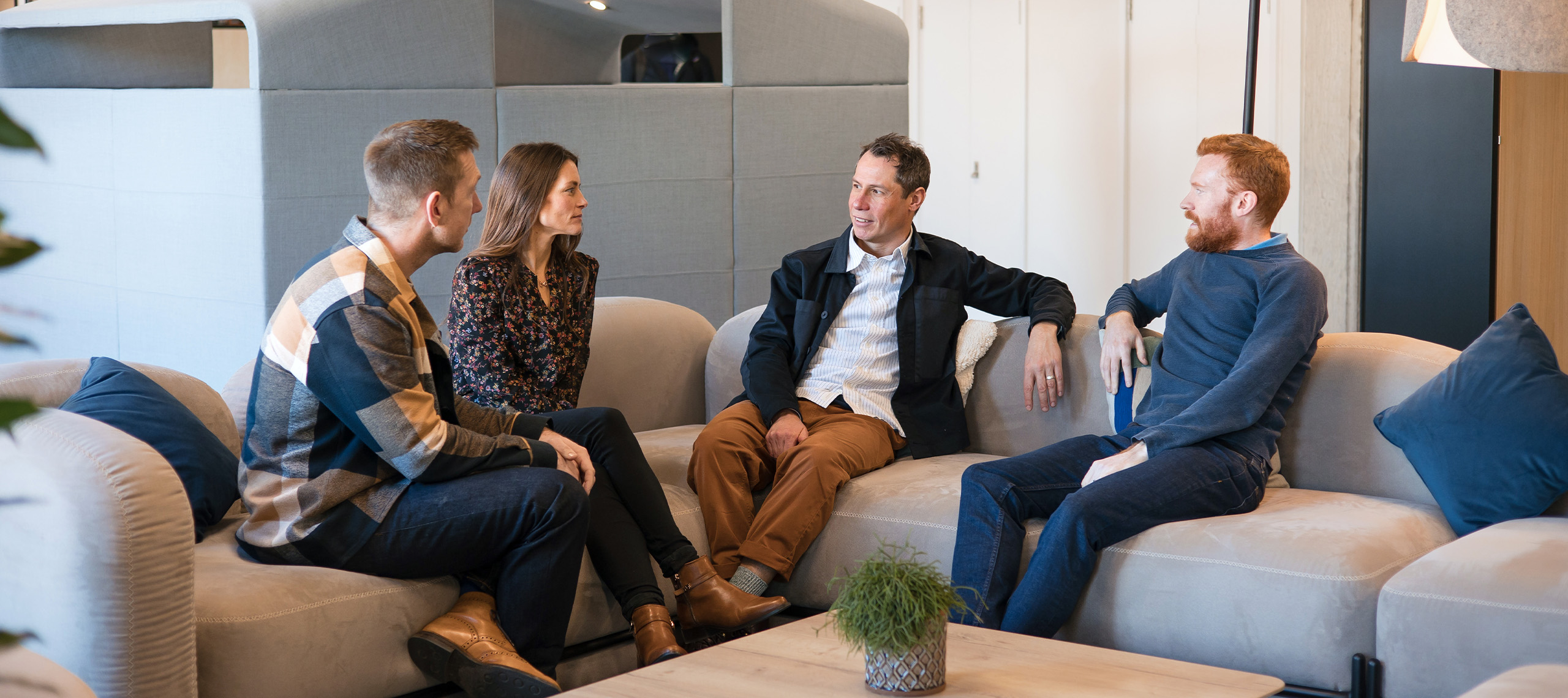 3 men and 1 women sitting on a sofa in a communal area of an office