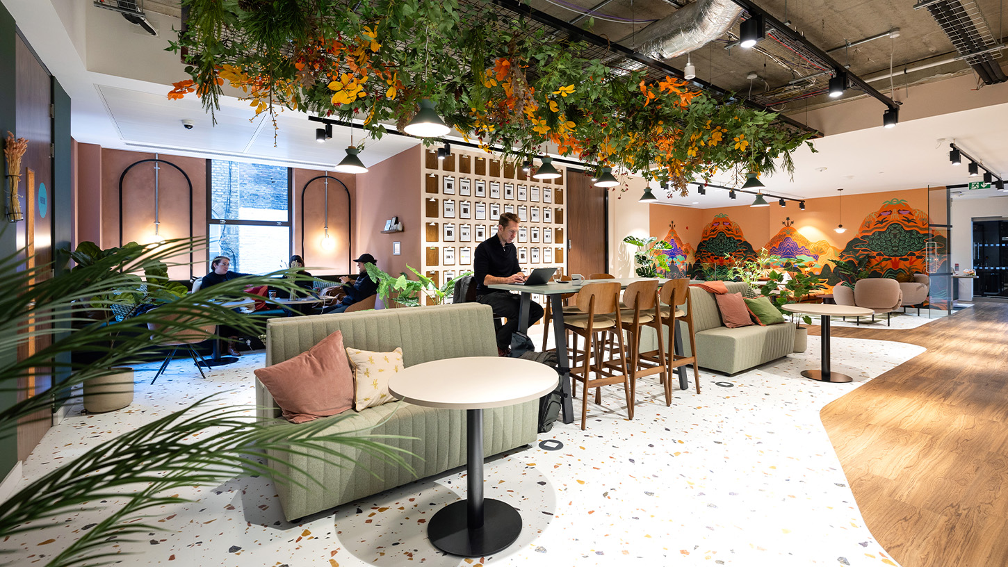 Communal working area with soft seating, high workbenches and man working at a laptop