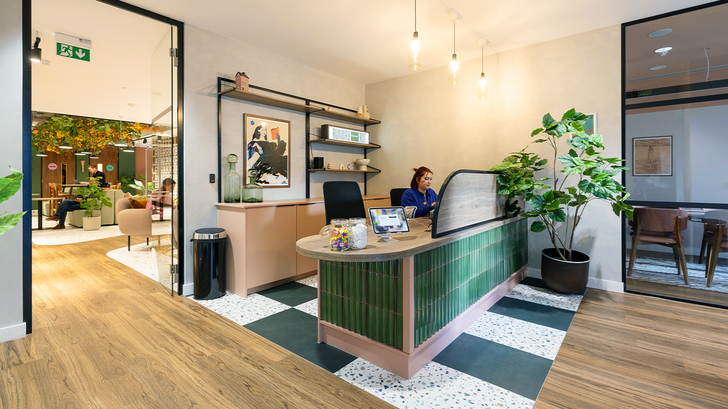 Welcoming reception area with green tiles and plants, one reception worker sits at her desk
