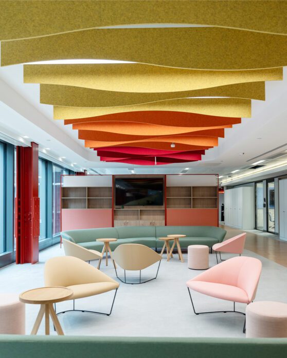 A bright and open seating area with pastel coloured chairs and bright yellow, orange and red acoustics on the ceiling