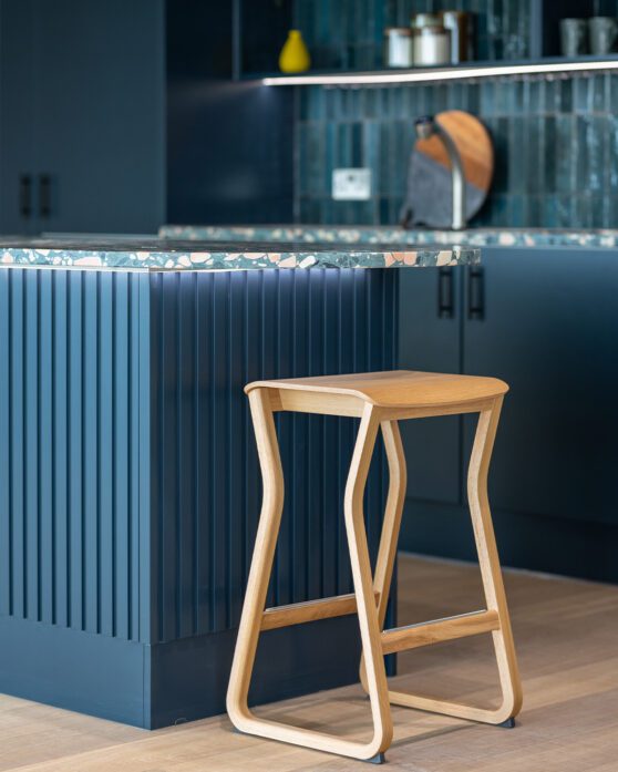 Bold blue kitchen with blue terrazzo countertop with a single light wood stool