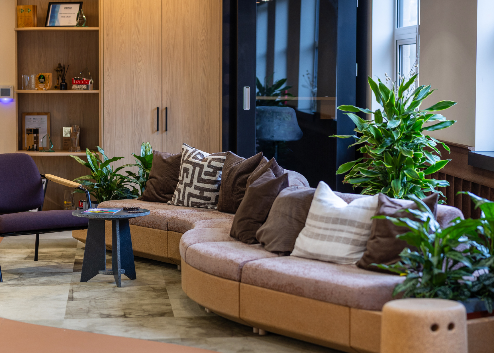 Curved cork sofa with purple and brown cushions and indoor planting