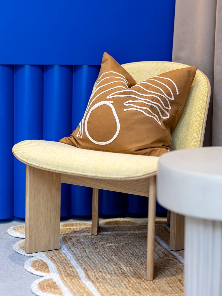 A closeup of a wood armchair in neutral tones with a light brown cushion against an electric blue reception desk
