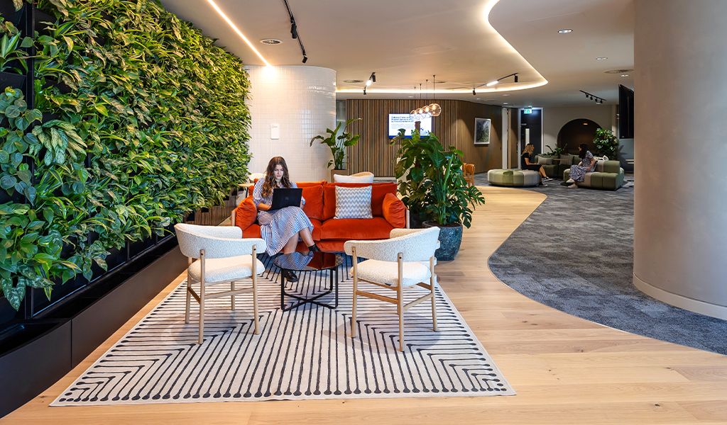 A woman sat on her laptop in a cosy lounge area with a living plant wall next to her