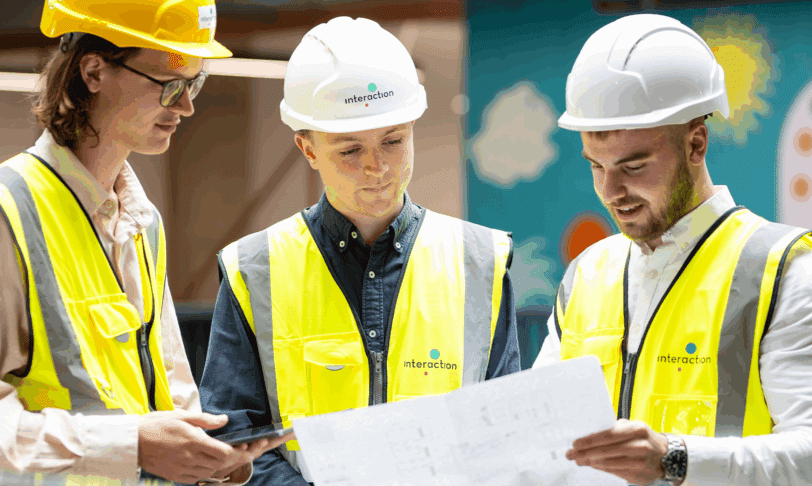 Three men in hivis and hard hats are looking at building plans together