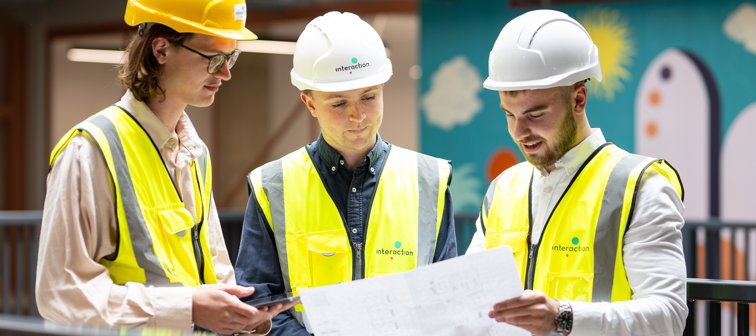 Three men in hivis and hard hats are looking at building plans together