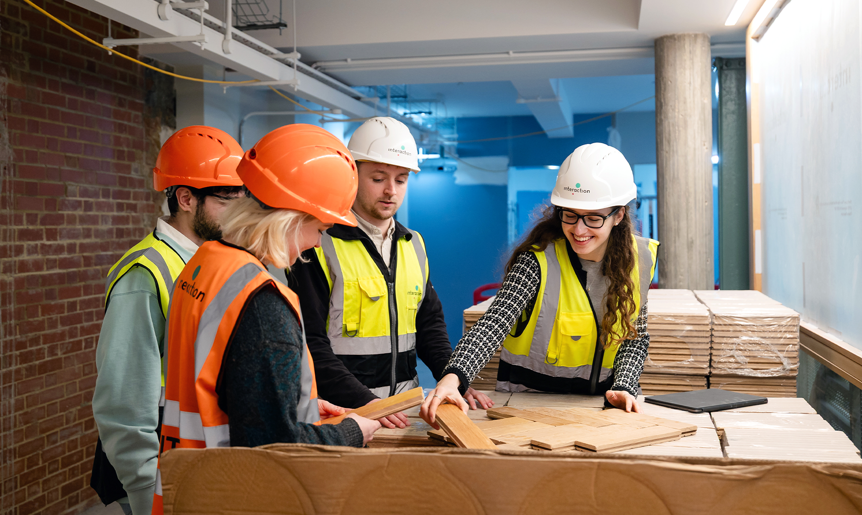 four people in hi-vis and hard hats looking at oak parquets floor tiles together