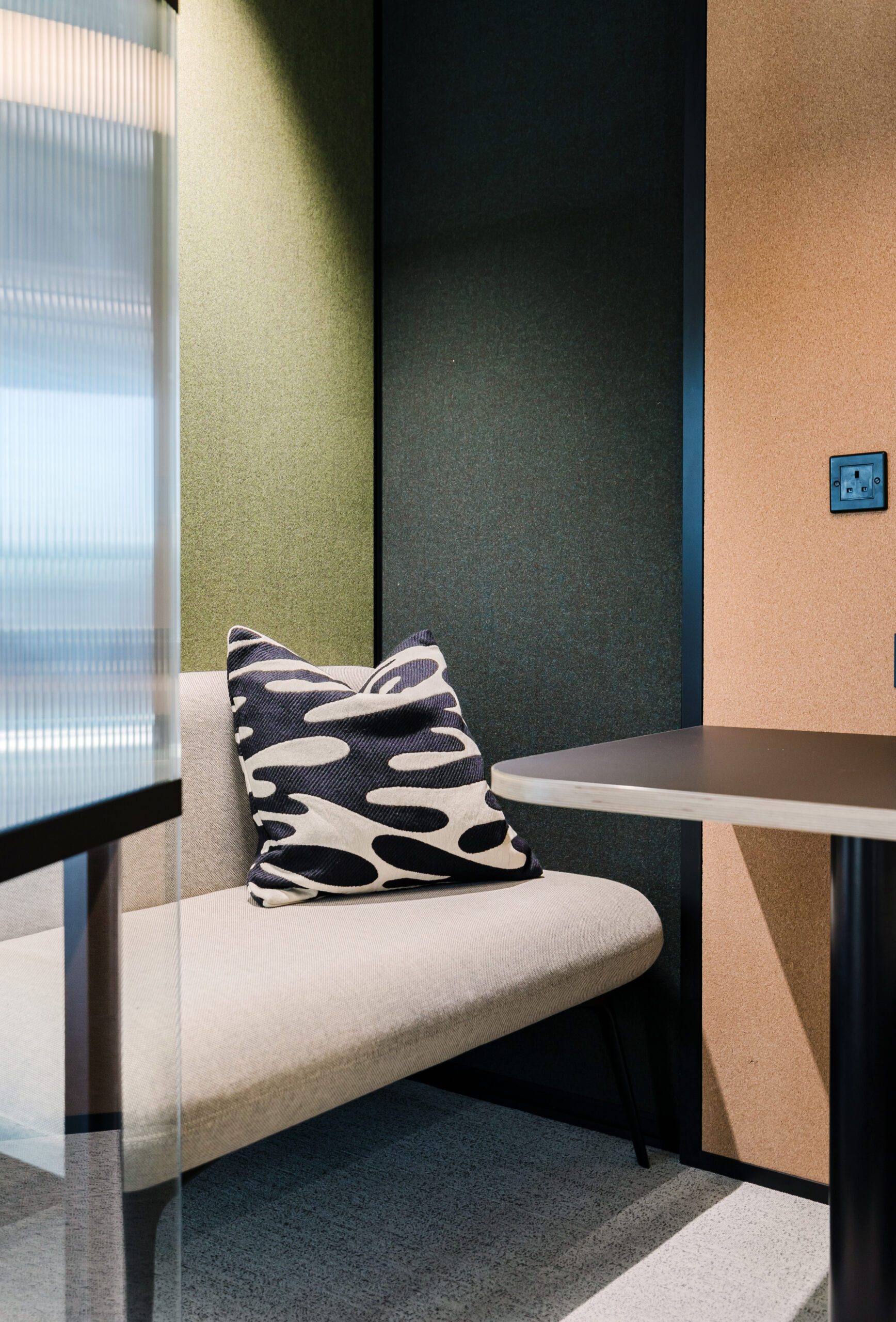 An office focus booth with soft green acoustic walls and grey banquette seating