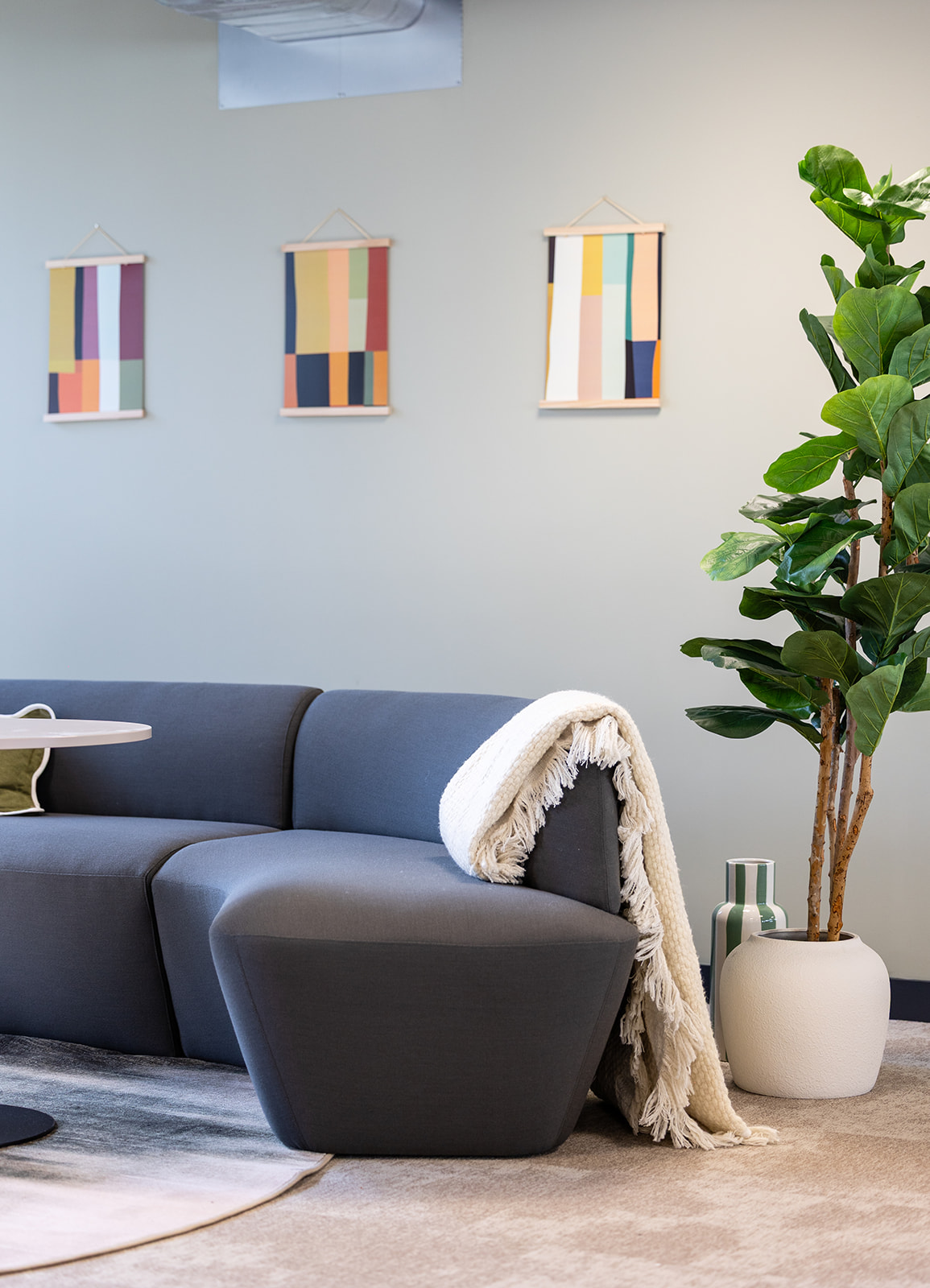 A blue sofa against a green wall with 3 colourful paintings