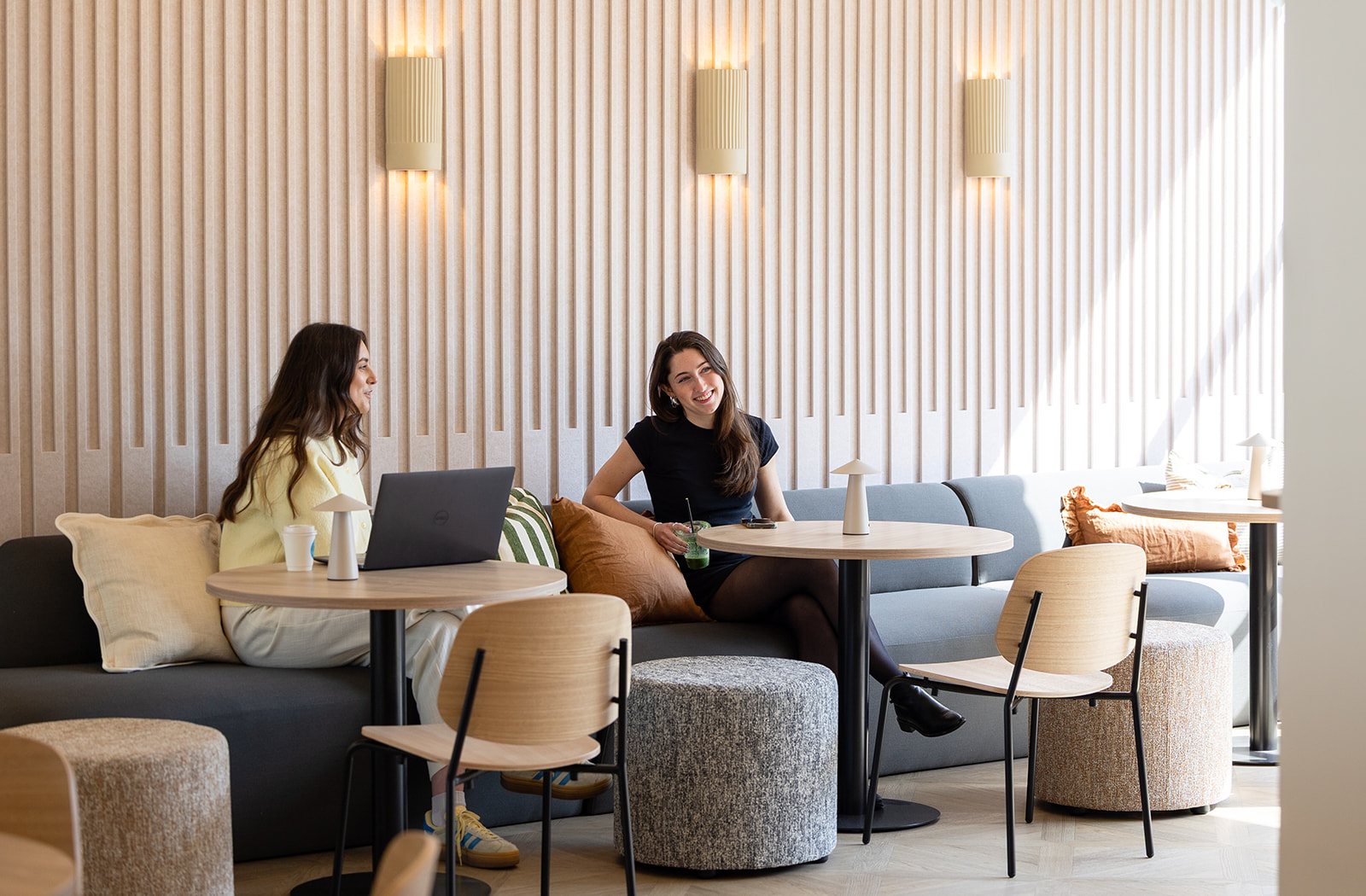 Two women talking on casual sofas against a neutral backdrop