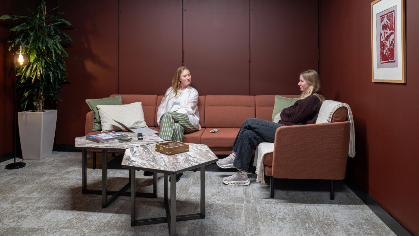 A cosy meeting area with earthy mauve walls and a large comfortable teracotta corner sofa.