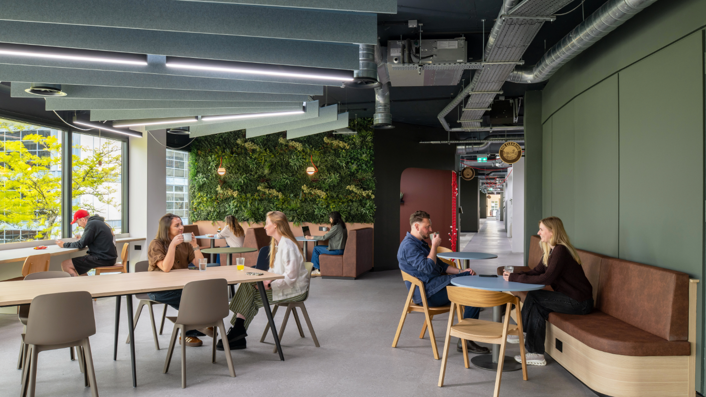 An open social area with a plant wall, tables and chairs and a mauve feature wall.