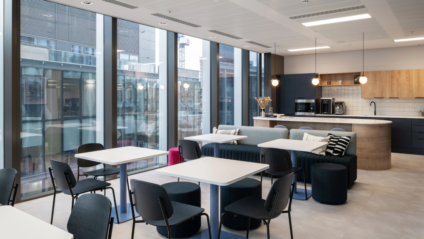 An open plan breakout space in the kitchen, with lots of tables and chairs, and floor to ceiling views of the city.