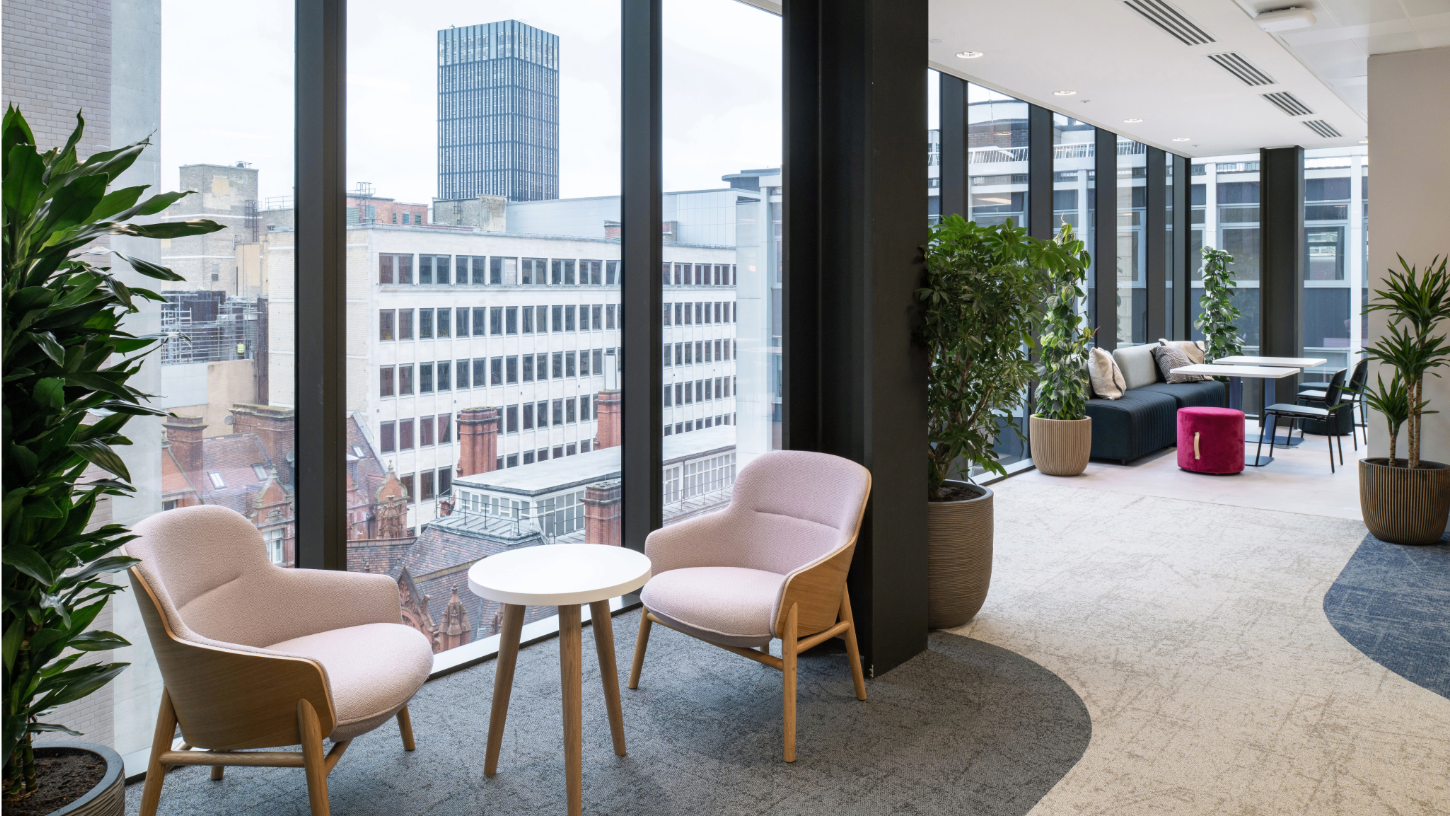 Soft pink seating next to floor to ceiling windows looking over views of the city, with green foliage and warm blue carpets.