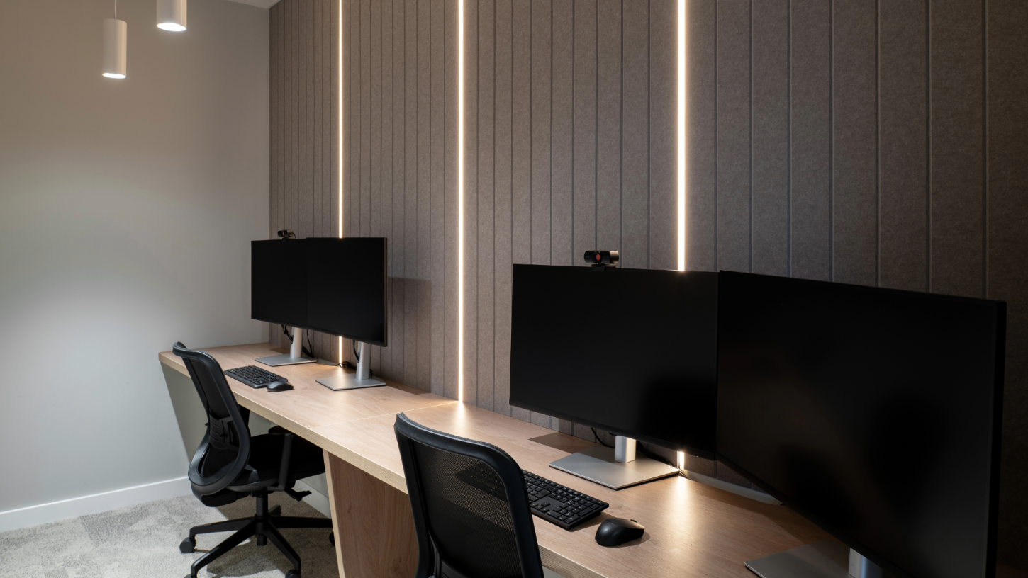A large virtual hearing room with wide desks and multiple screens, soft natural acoustic wall panelling and strip lighting to illuminate the walls.